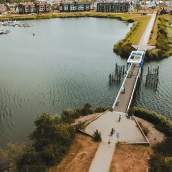 Brug over een Maasplas met wandelaars en fietsers, met woningen aan het water op
